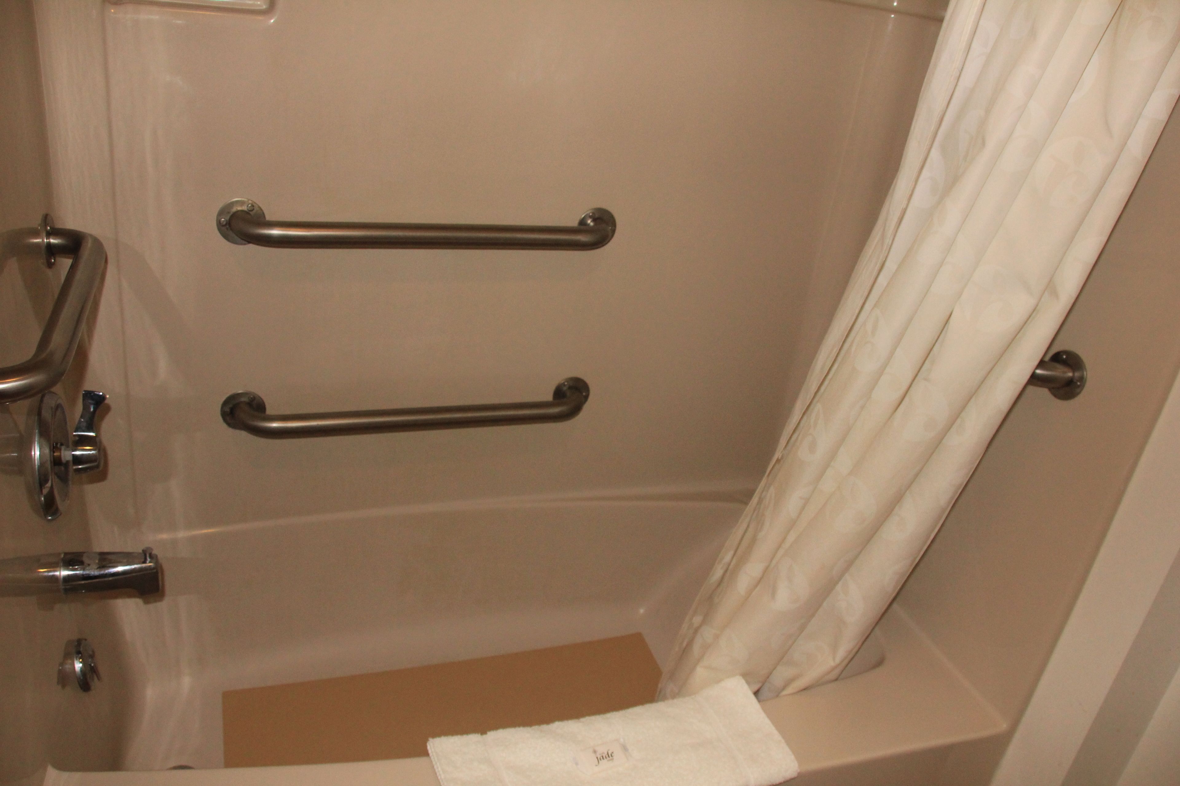Baño con bañera, dos barras de apoyo, una toalla y una cortina.