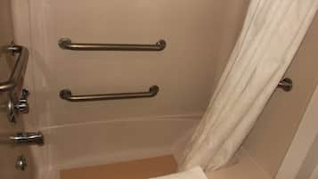 Baño con bañera, dos barras de apoyo, una toalla y una cortina.