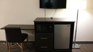 Une chambre compacte équipée d’un bureau, d’une chaise, d’un téléviseur à écran plat, d’un four à micro-ondes et d’un réfrigérateur.