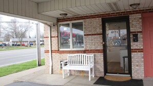 Un bâtiment avec une façade en briques, un banc blanc à l’extérieur et une porte sur laquelle on peut lire les inscriptions « OUVERT » et « BUREAU ».