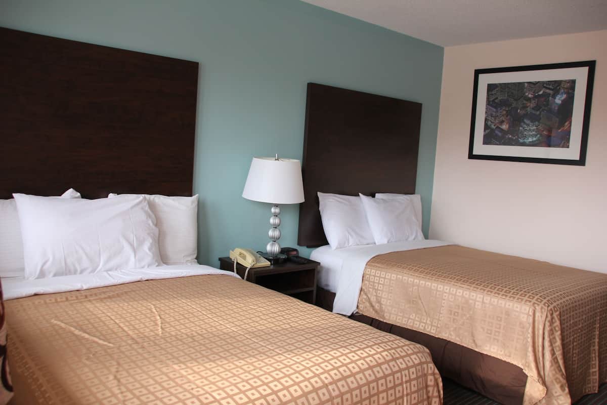 A hotel room with two beds, a nightstand with a lamp, a phone, and a framed picture on the wall.