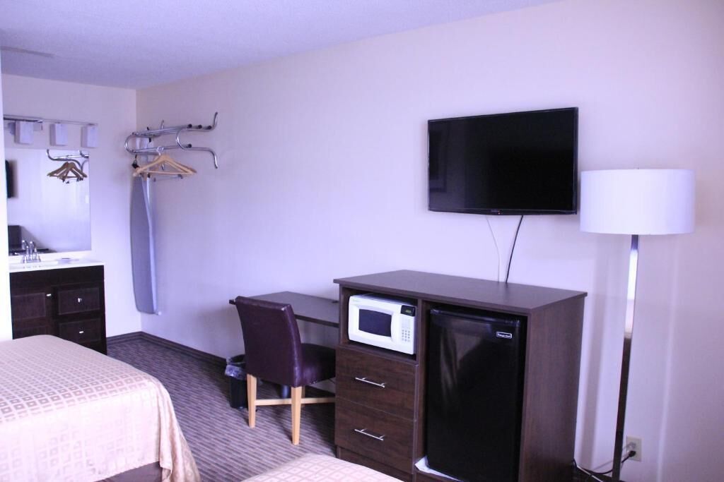 A hotel room with a bed, a desk with a microwave, a TV, and a lamp.