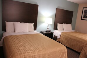 Habitación de hotel con dos camas, cada una con cabecero, mesita de noche con lámpara y un cuadro en la pared.