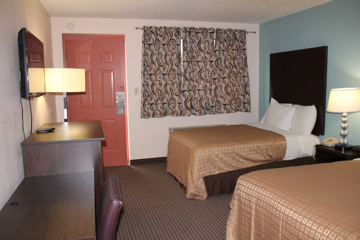 A hotel room with a bed, a desk, a chair, a telephone, and a curtain.