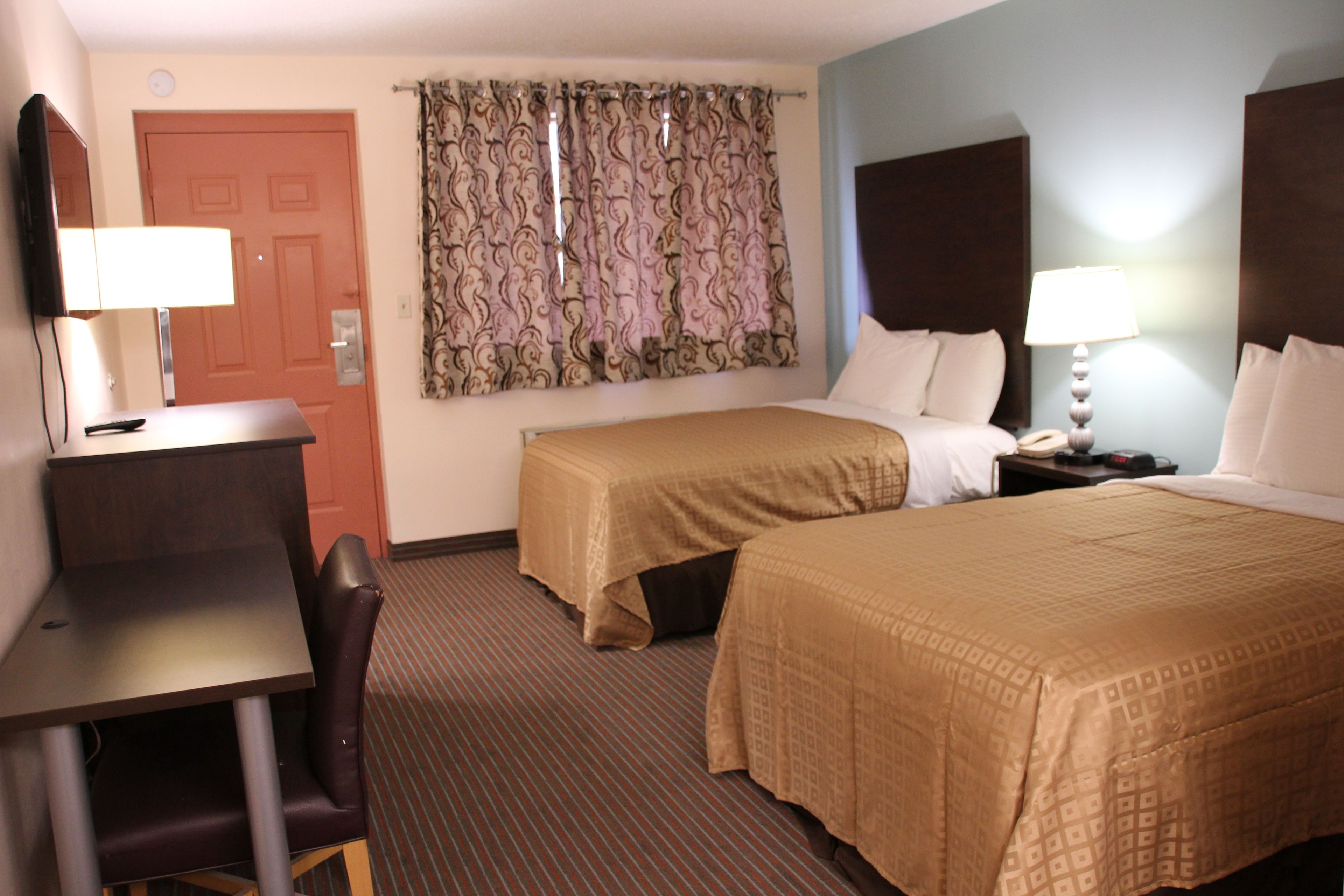 A hotel room with a desk, two beds, a TV, and a window with curtains.