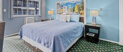 A bedroom with a large bed, two bedside tables with lamps, a window with curtains, and a painting on the wall.