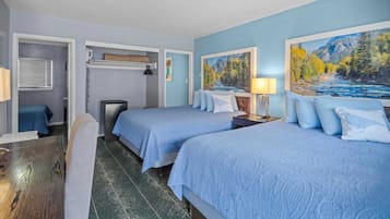 A hotel room with two beds, a desk, and a chair. There are paintings on the walls and a window with blinds.