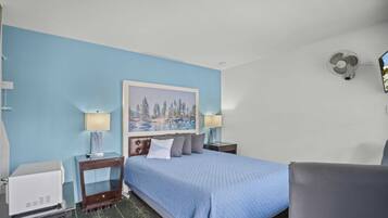 A hotel room with a bed, two bedside tables, a chair, a desk, a lamp, a painting, and a wall-mounted fan.