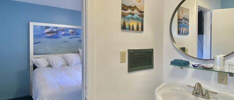 A hotel room with a bed, a bathroom with a sink and mirror, and a painting on the wall.
