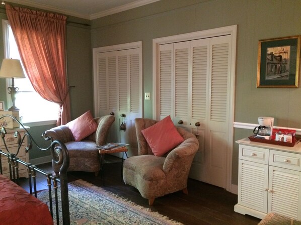 A cozy room with two armchairs, a small table, a cabinet with drawers, and a window with curtains.