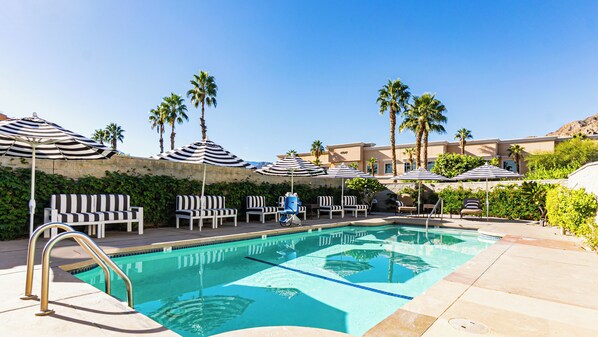 A pool area with lounge chairs, striped umbrellas, and palm trees. - The Chateau at Lake La Quinta (La Quinta)