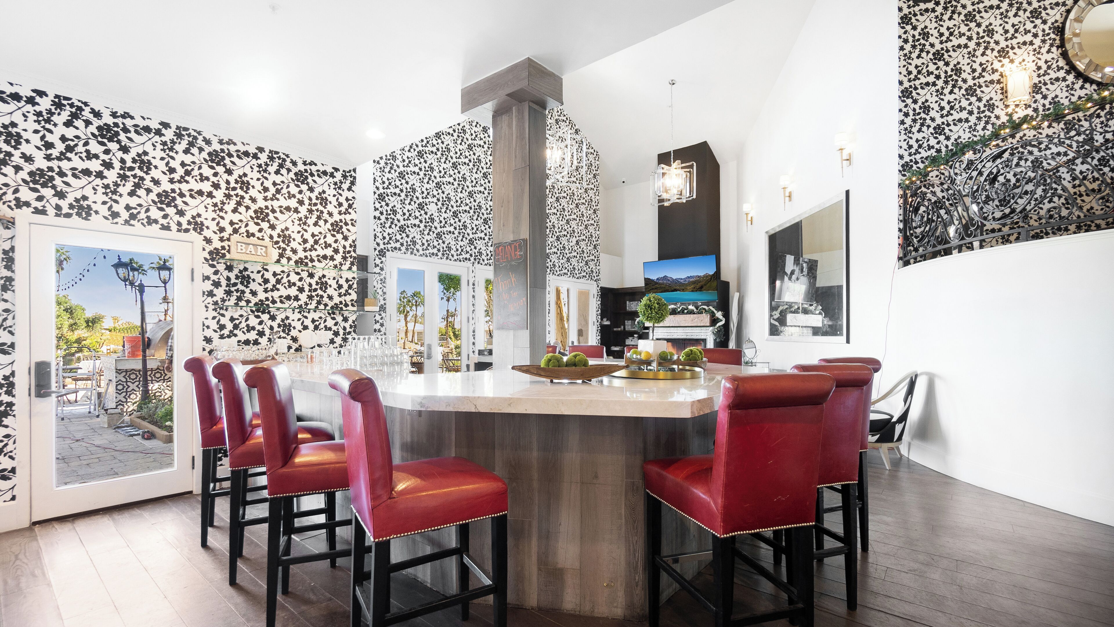 A modern kitchen with a central island, red bar stools, and a view of the outdoors.