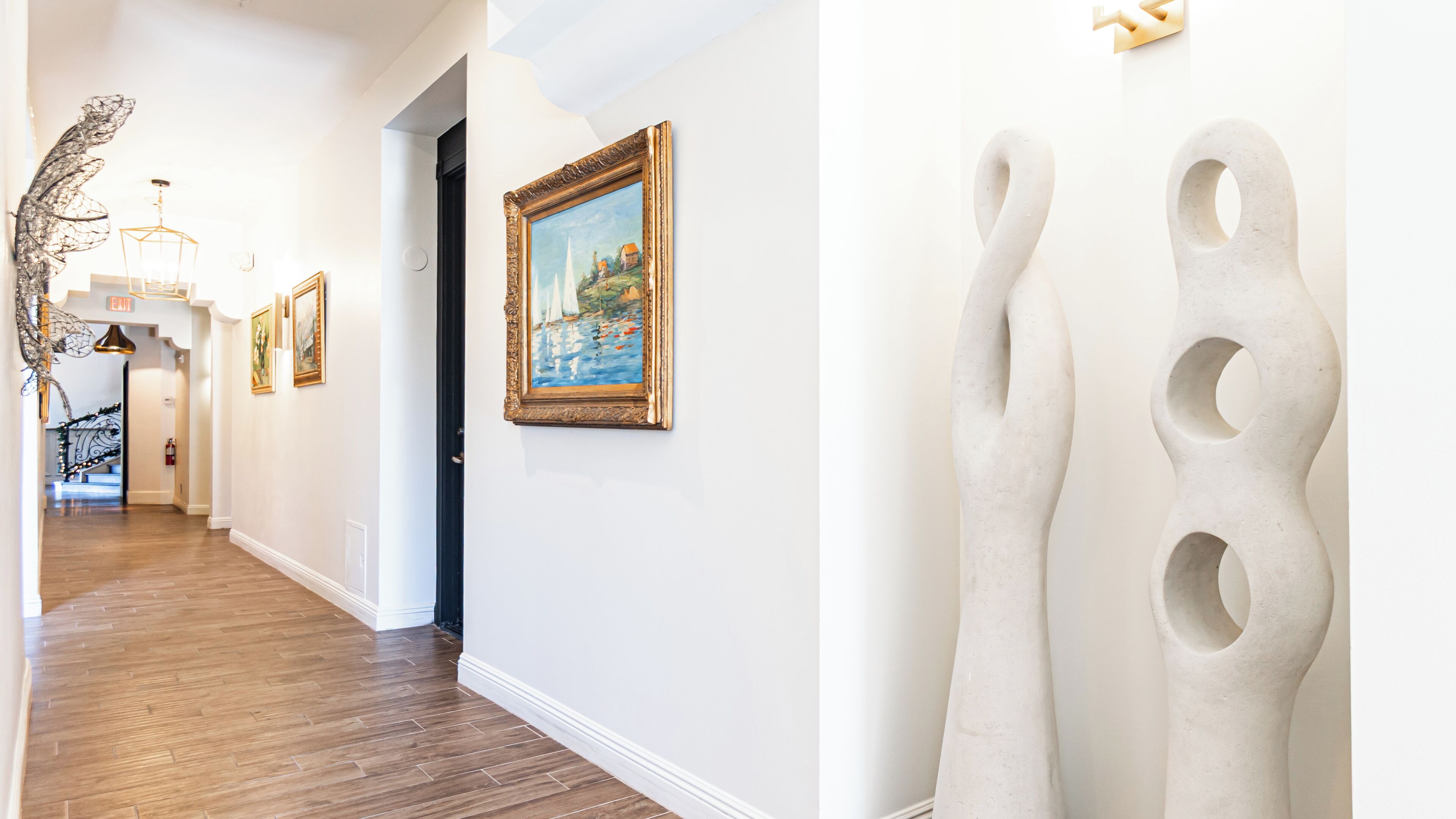 A hallway with wooden flooring, a painting on the wall, and a sculpture.