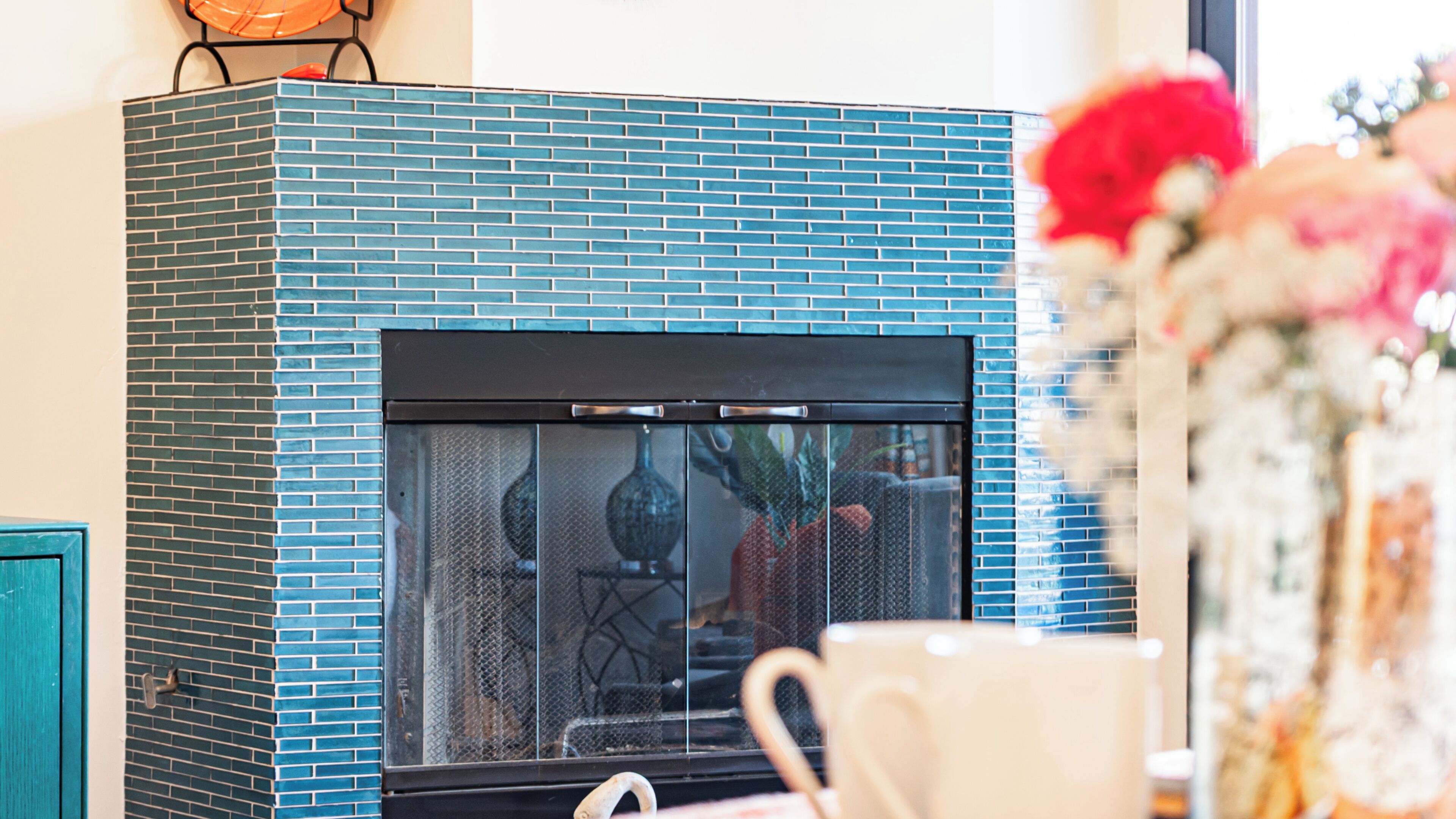 Une cheminée avec un foyer orné de carreaux bleus et une porte en verre noir.