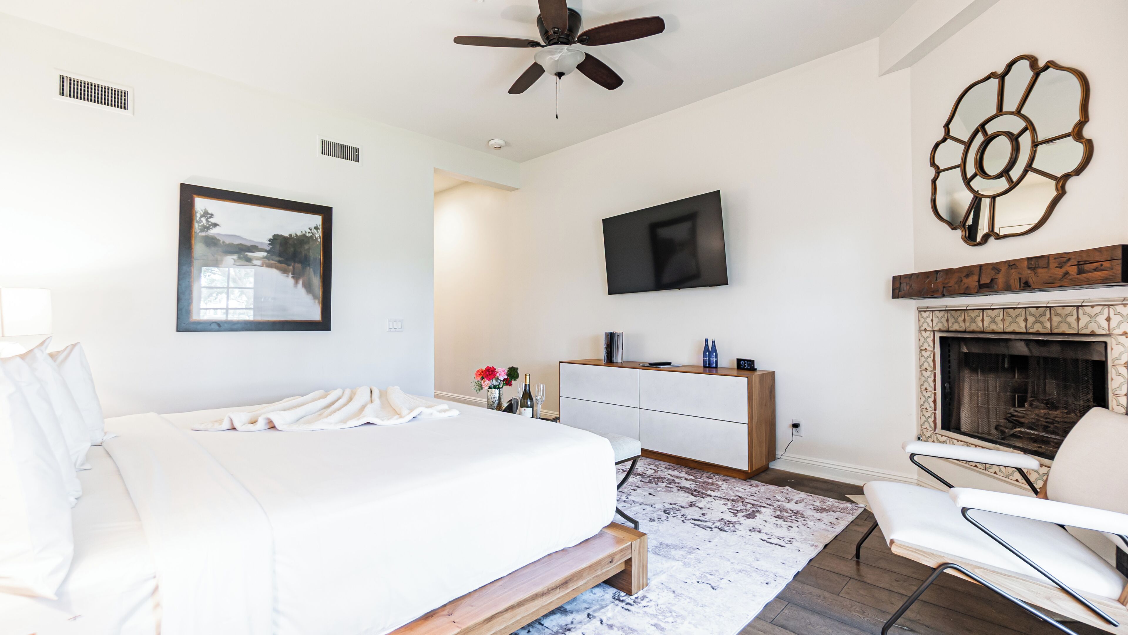 Un dormitorio moderno con una cama grande, televisor, chimenea y un elemento decorativo en la pared.