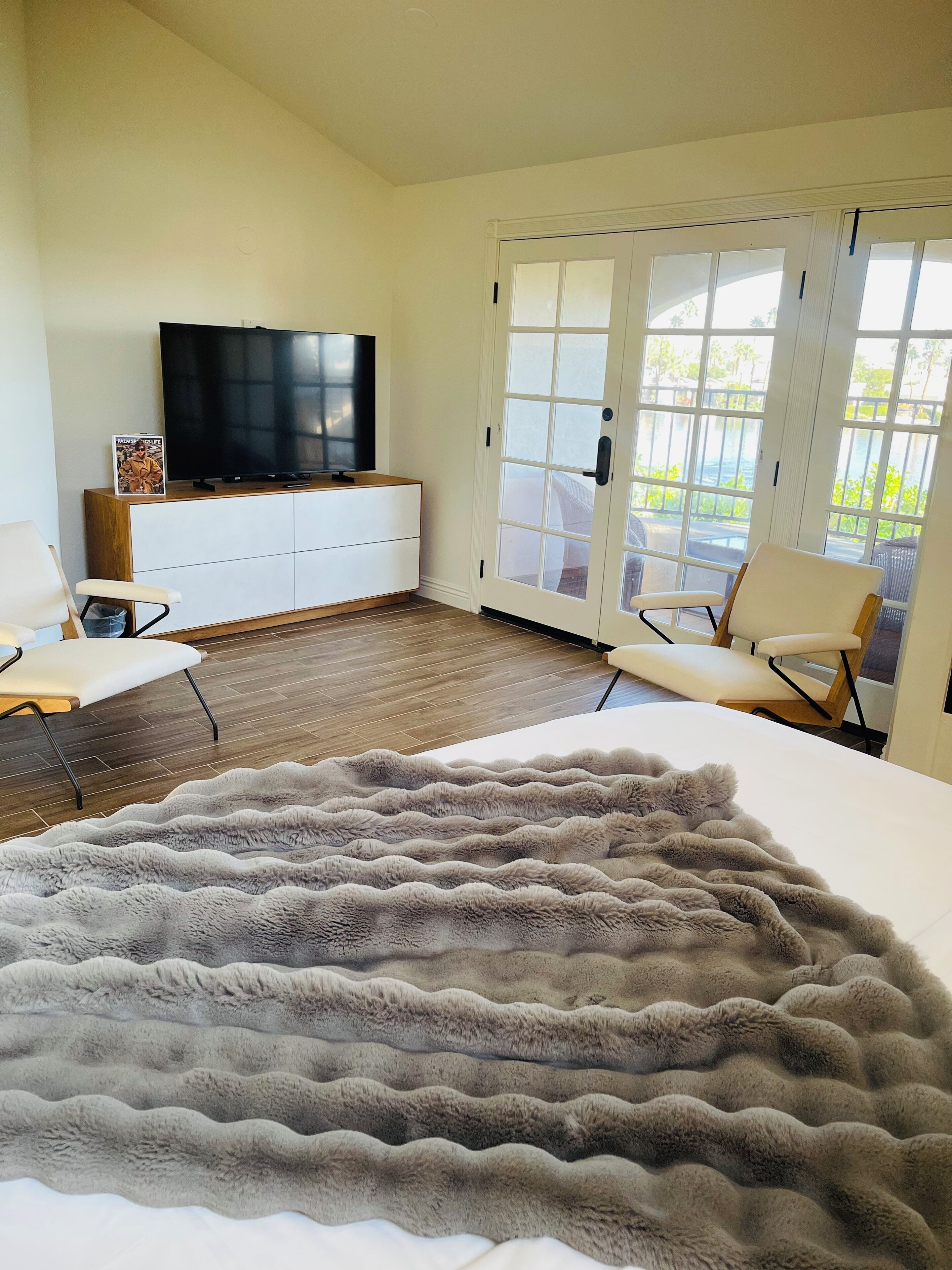 Quarto com um tapete grande e fofo, uma TV sobre um móvel de madeira e uma porta de vidro deslizante para uma varanda.
