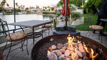 An outdoor seating area with a fire pit, tables, chairs, and a view of a body of water.