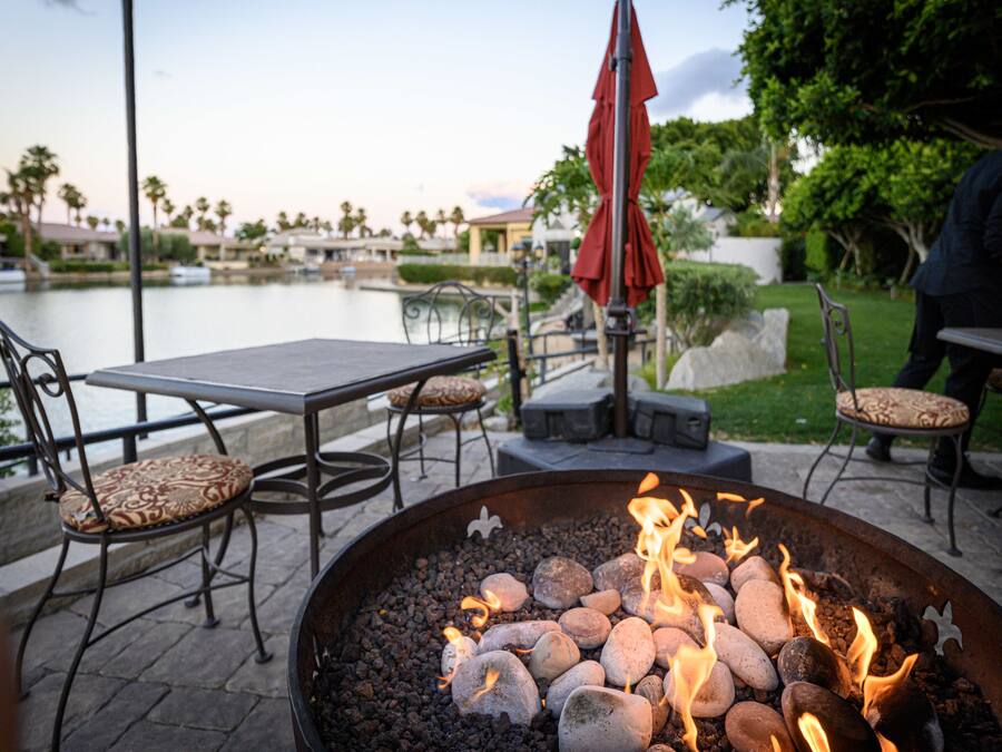 An outdoor seating area with a fire pit, tables, chairs, and a view of a body of water.