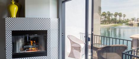 A balcony with wicker furniture, a fireplace with a patterned wall, and a view of a body of water and palm trees.