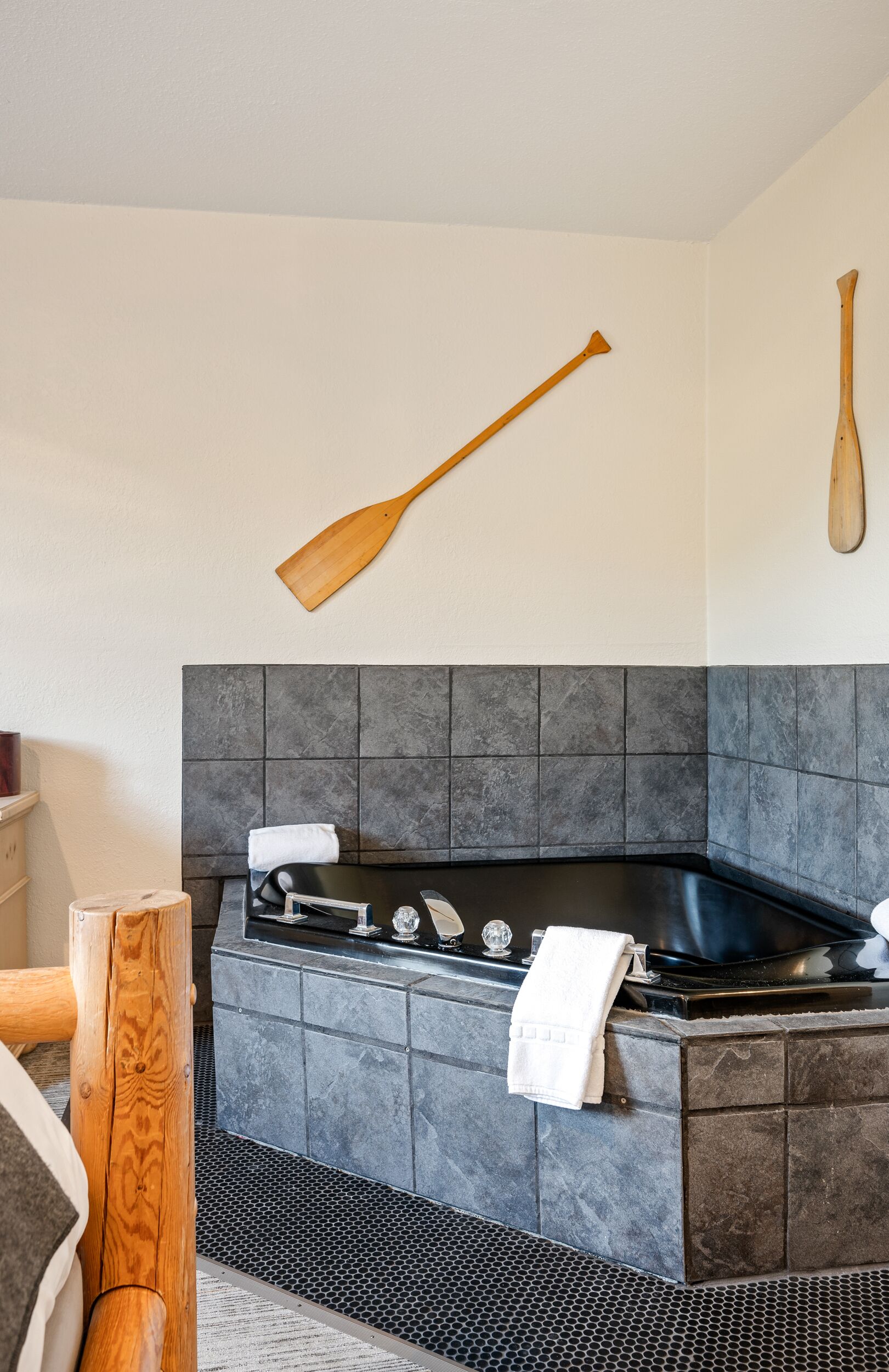 A modern bathroom with a black bathtub, a wooden paddle, and a towel hanging on the wall.