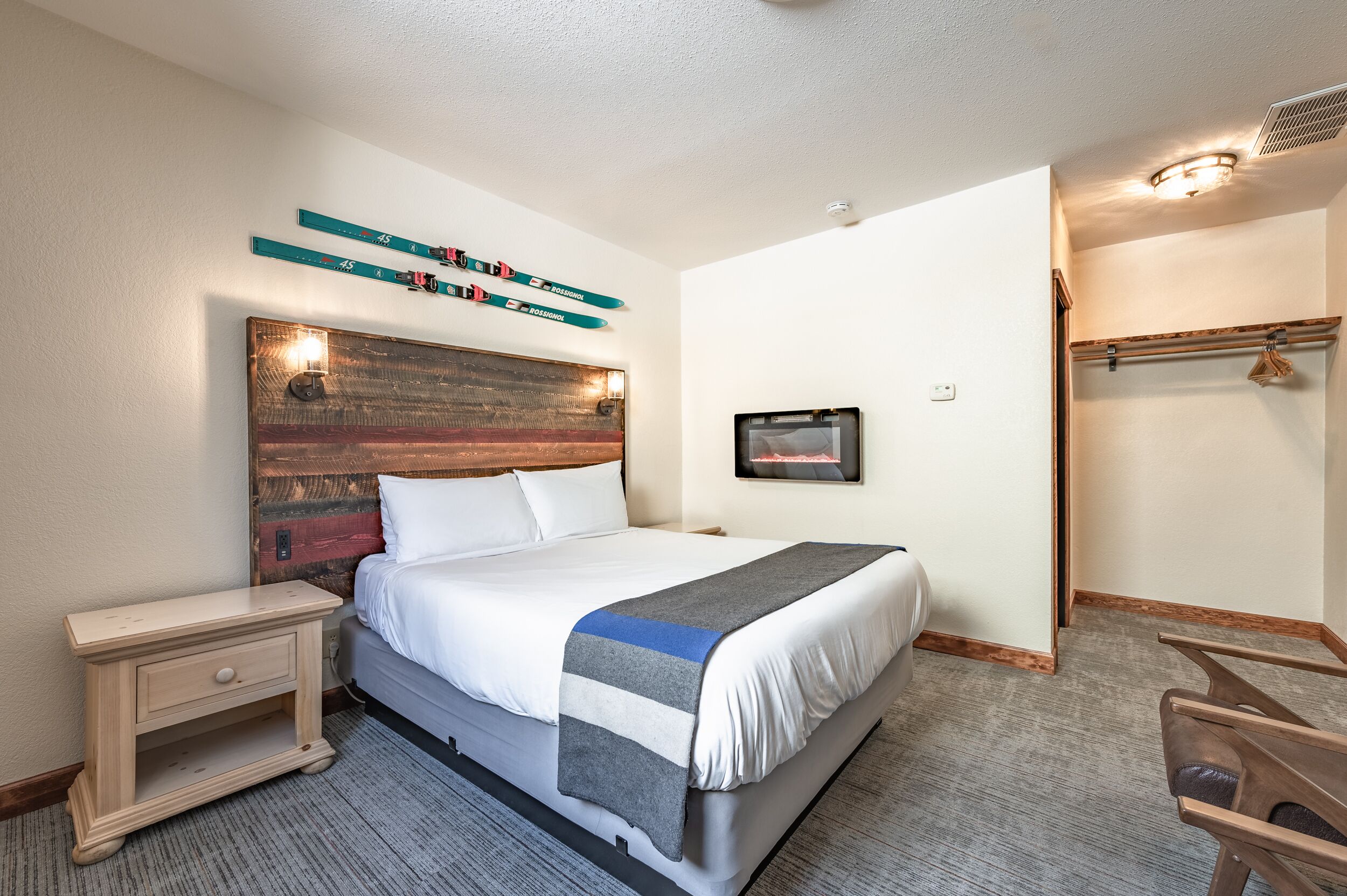 Une chambre d’hôtel équipée d’un lit, d’une table de chevet, d’un porte-skis fixé au mur et d’un porte-manteau.