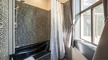 A modern bathroom with a black bathtub, a shower with a rain showerhead, and a window with a view of trees.