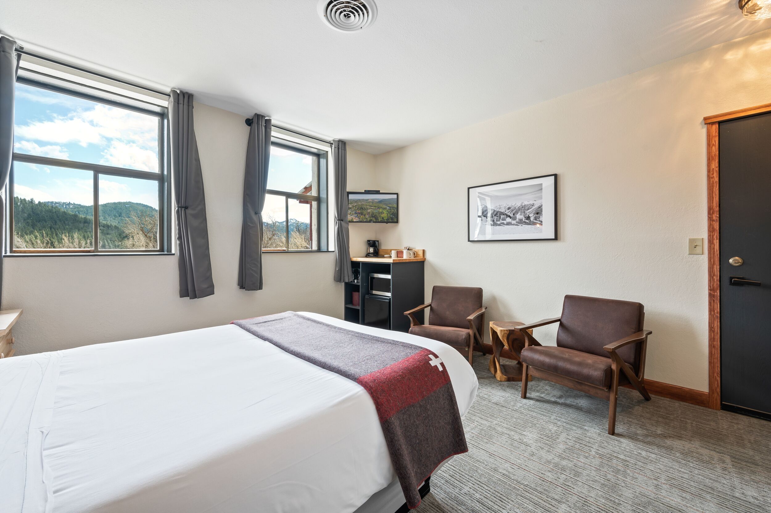 Ett hotellrum med en stor säng, två stolar, ett skrivbord med en dator och en tv på väggen.