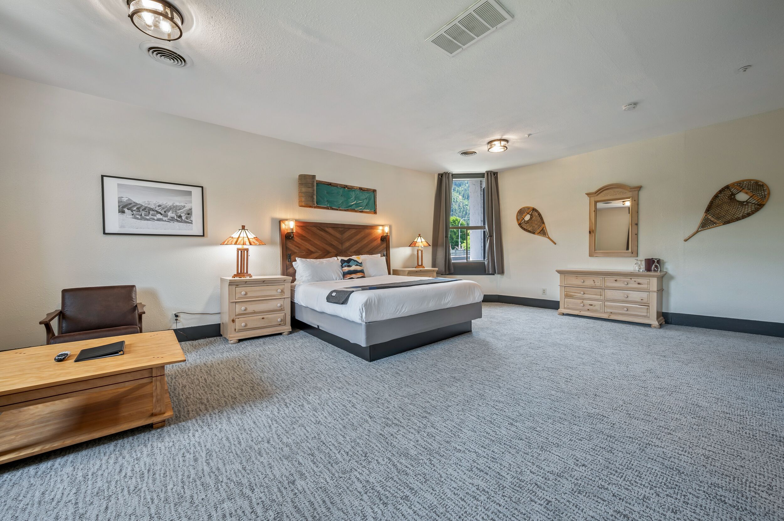 A hotel room with a bed, desk, chair, bedside tables, lamps, and decorative wall art.