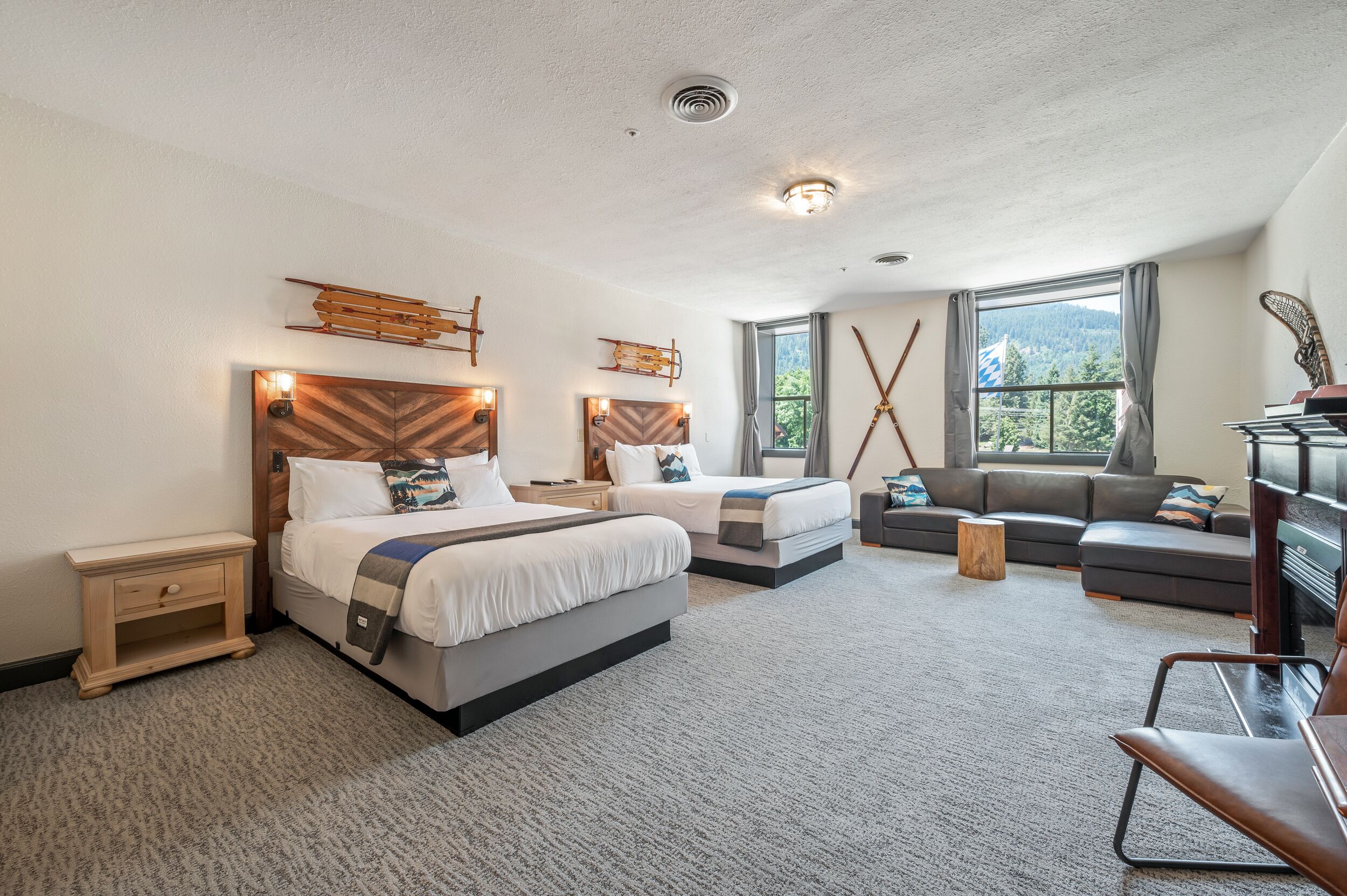 Quarto de hotel com duas camas, um sofá, uma televisão e uma janela grande com vista para o exterior.