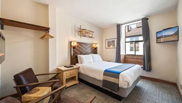 Habitación de hotel con cama, mesita de noche de madera, silla y vista a un edificio por la ventana.