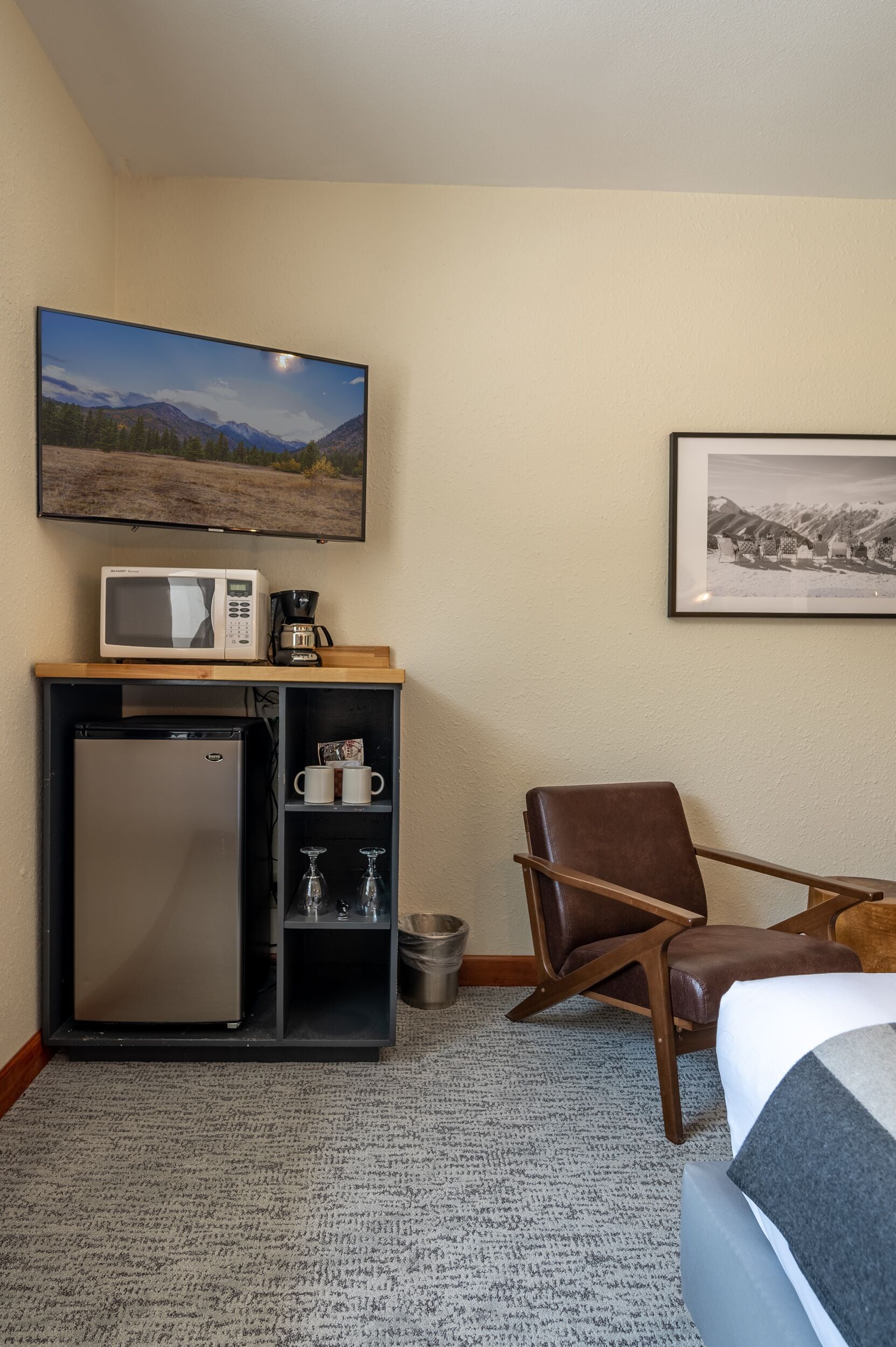 A hotel room with a bed, a desk with a microwave, a refrigerator, a chair, a picture on the wall, and a framed photo.