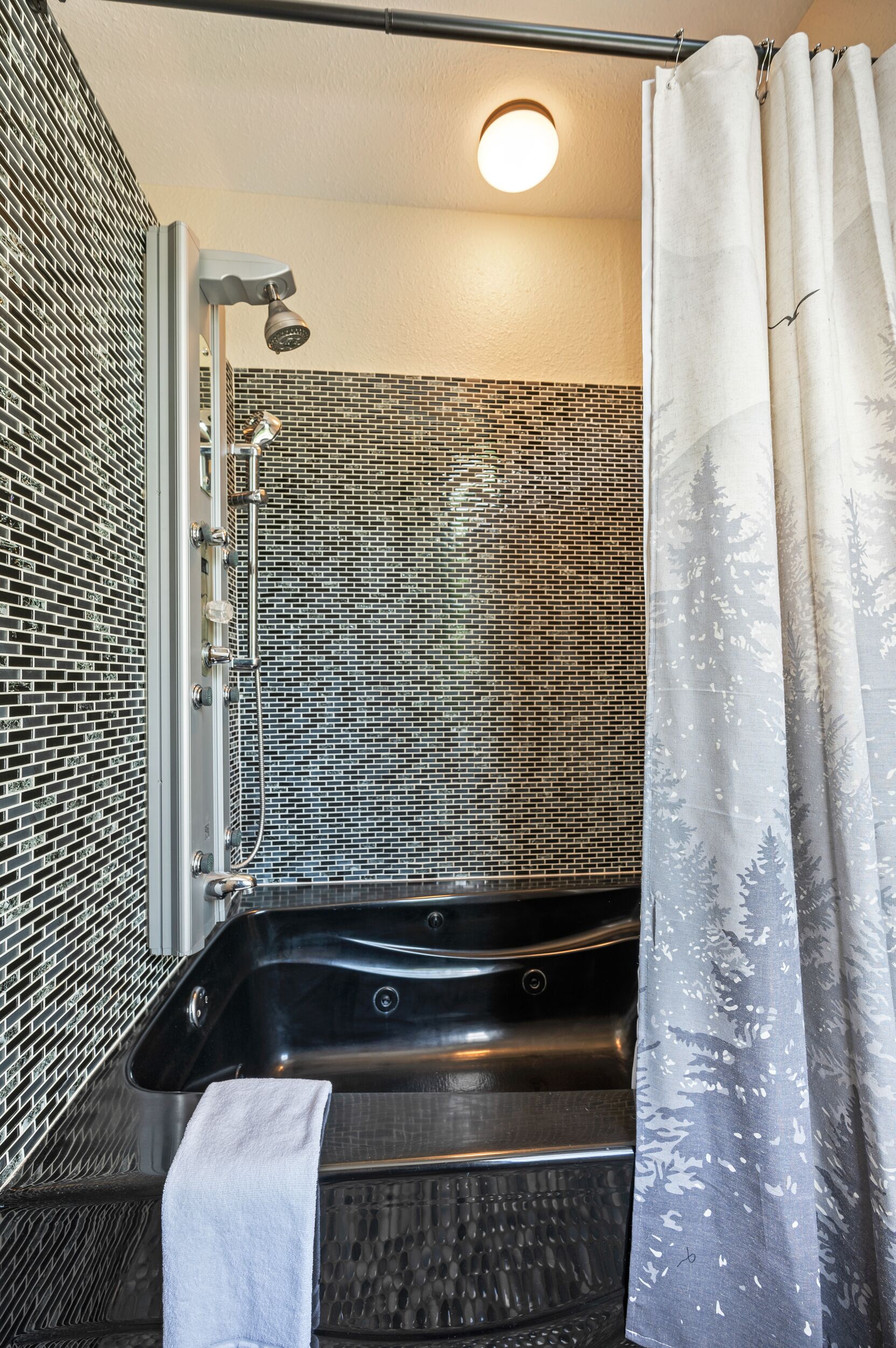 A bathroom with a black bathtub, a shower, and a tiled wall.