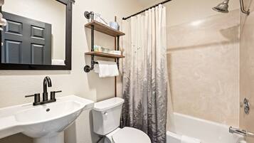 Une salle de bain équipée d’un lavabo, de toilettes et d’une baignoire. Une étagère se trouve au-dessus des toilettes, où sont rangés les articles de toilette.