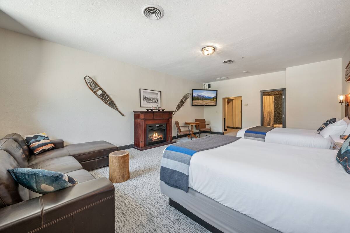 Quarto de hotel com lareira, sofá, duas camas e televisão.