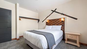 A neatly made bed with a grey blanket, a wooden headboard, and a bedside table with a drawer.