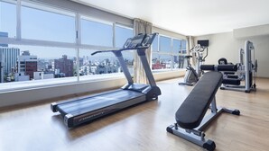 A gym with a treadmill, bench, and weight machines, large windows with a city view. - Exe Suites Reforma (Mexico City)