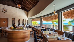 Ein Restaurant mit einer Holztheke, Tischen mit Stühlen und Blick auf den Ozean.