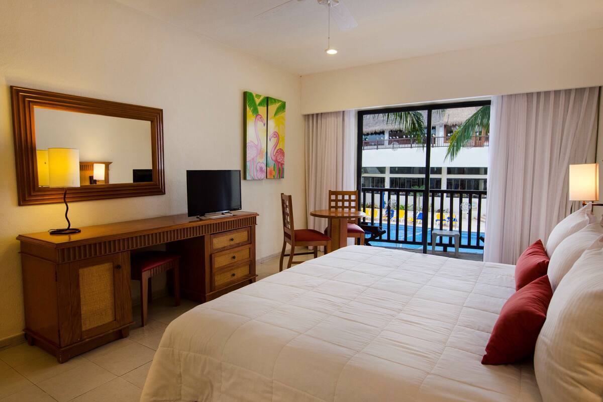Une chambre d’hôtel équipée d’un lit, d’un bureau, d’une chaise, d’une télévision et offrant une vue sur une piscine et un immeuble.