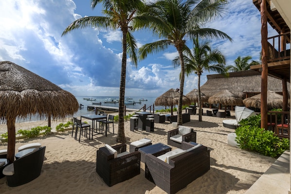 A beachside lounge with thatched umbrellas, wicker furniture, and a view of the ocean.