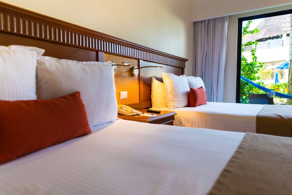 Une chambre d’hôtel avec deux lits, une tête de lit en bois, un téléphone sur la table de chevet et une vue sur l’extérieur.