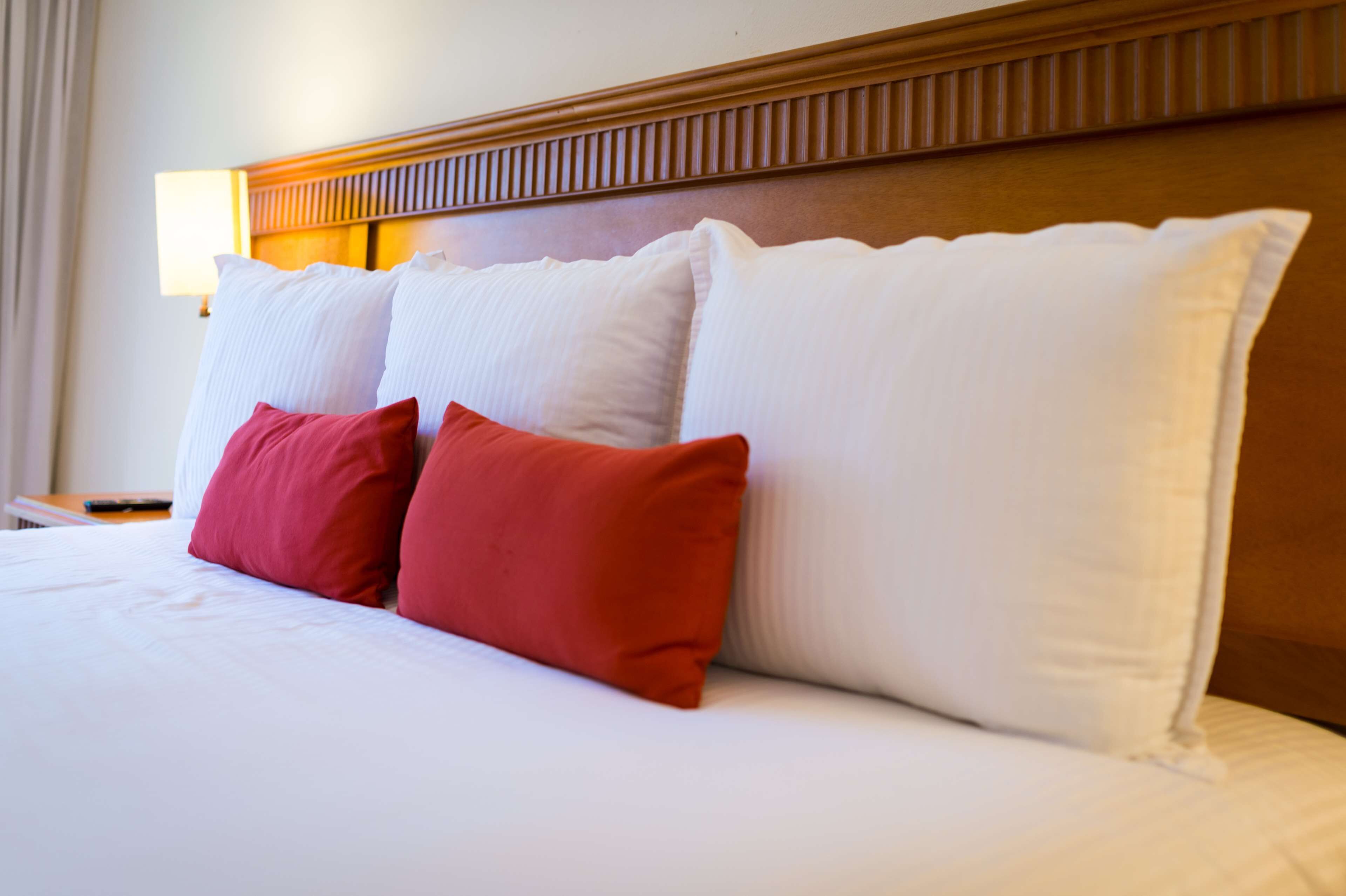 A neatly made bed with white and red pillows, a wooden headboard, and a bedside lamp.