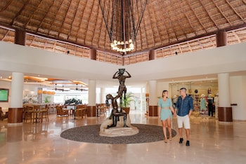 A bar area with a view of the sea, wooden chairs, and a thatched roof ceiling. at The Reef Coco Beach Resort & Spa- Optional All Inclusive