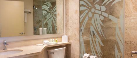 A bathroom with a marble sink, a toilet, a glass shower enclosure with palm leaf design, and a large mirror.