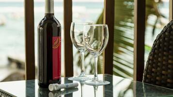 A table with a bottle of wine and two glasses on a glass table near a window overlooking the ocean.