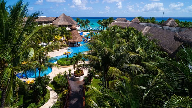 Ein Resort mit einem zentral gelegenen Pool, strohgedeckten Gebäuden und Blick auf den Ozean.