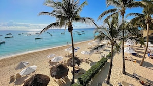 Ein Strand mit Palmen, Sonnenschirmen und Liegestühlen.