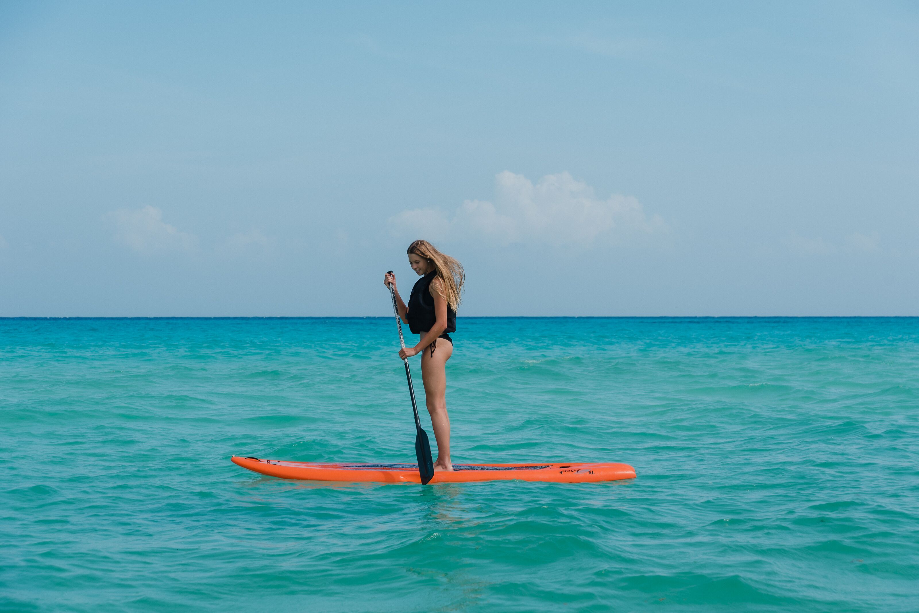 A person paddleboarding on a calm sea with clear skies.