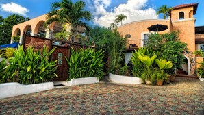 Un patio con sendero de ladrillo, palmeras y un edificio con arcos y techo de tejas.