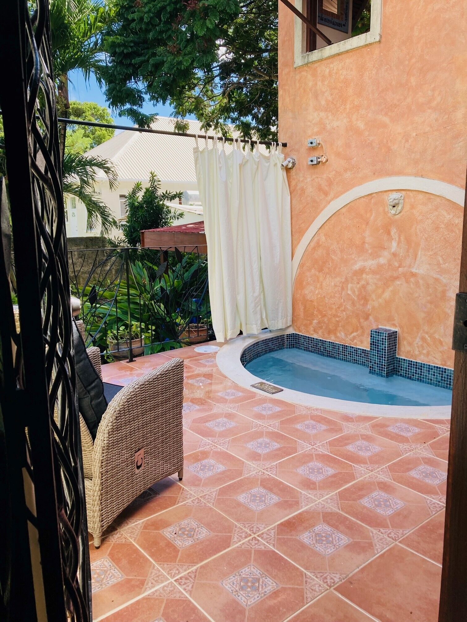 Una zona de piscina con suelo de baldosas, una silla de mimbre y una cortina blanca.
