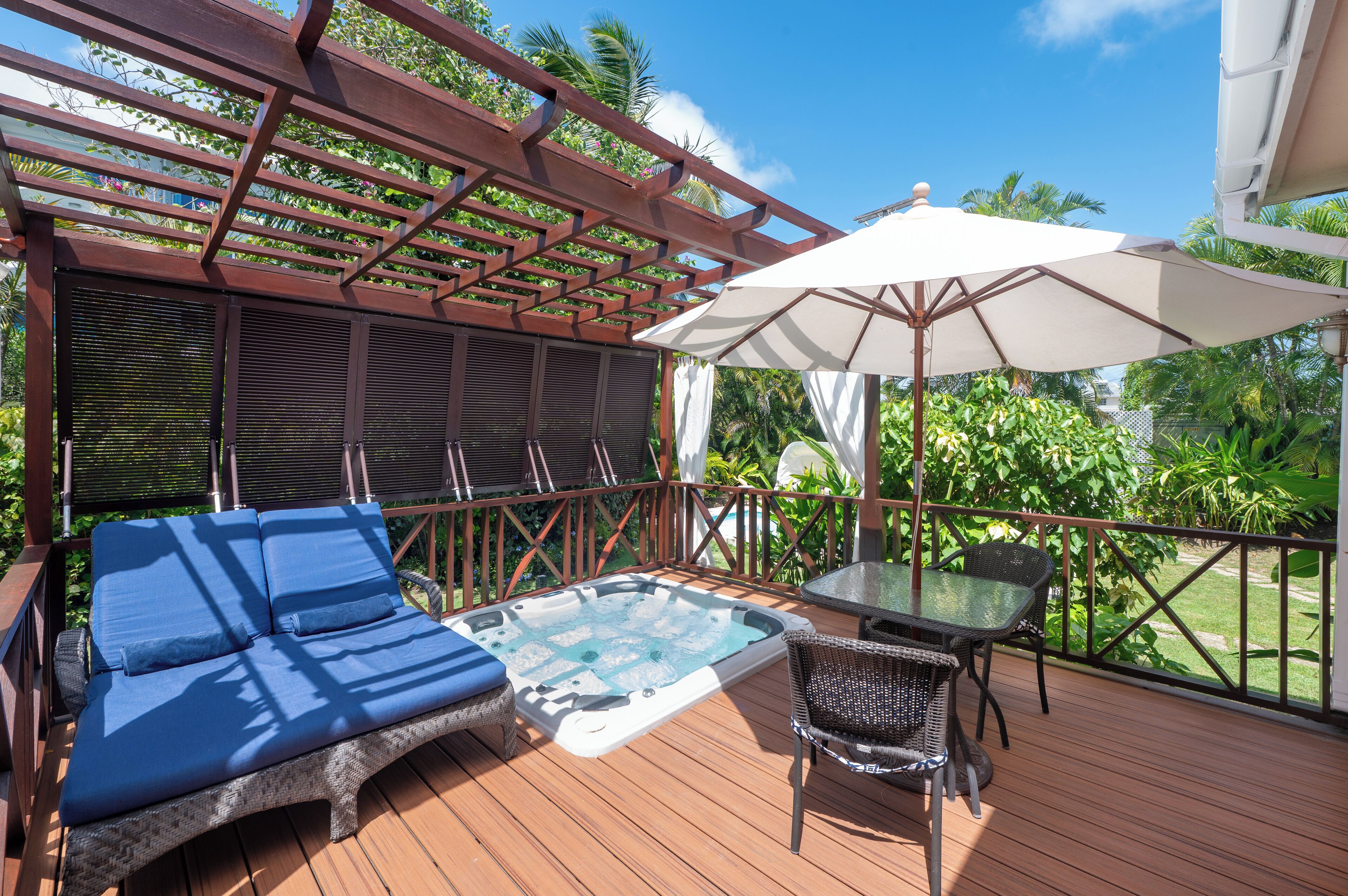 Una terraza de madera con un jacuzzi, una silla de descanso y una mesa con sombrilla.